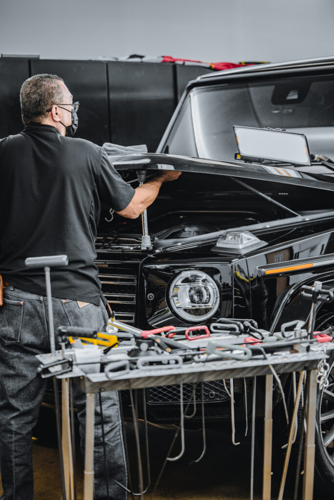 Sal working on fixing a dent on the hood of a black Mercedes Wagon